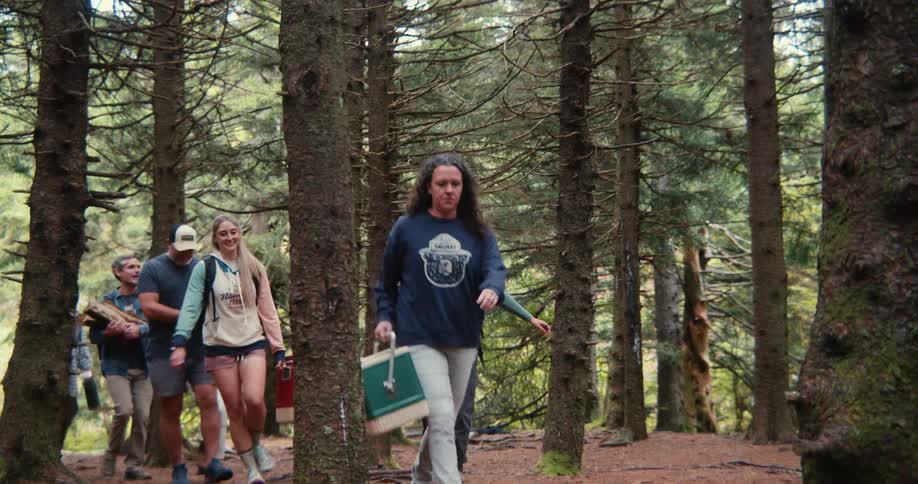 Group of friends hiking in a forest carrying firewood backpacks and coolers