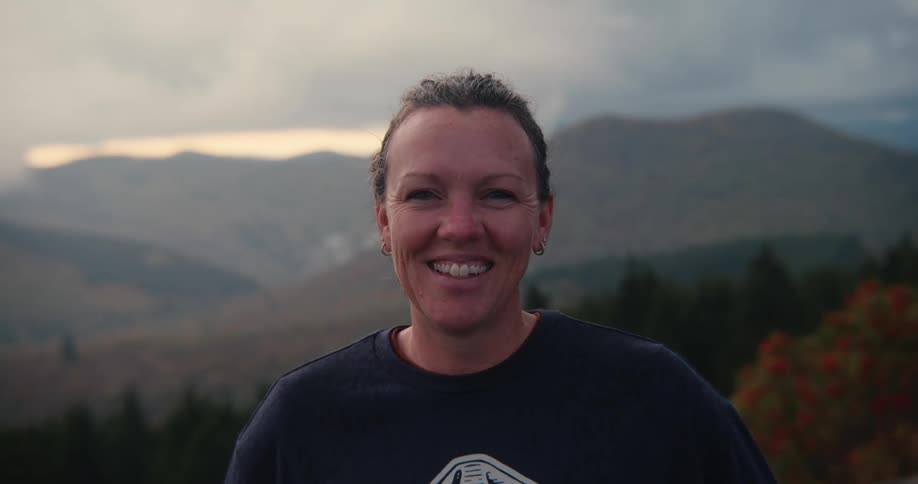 A woman standing before a scenic backdrop of valleys and mountains wearing a smile