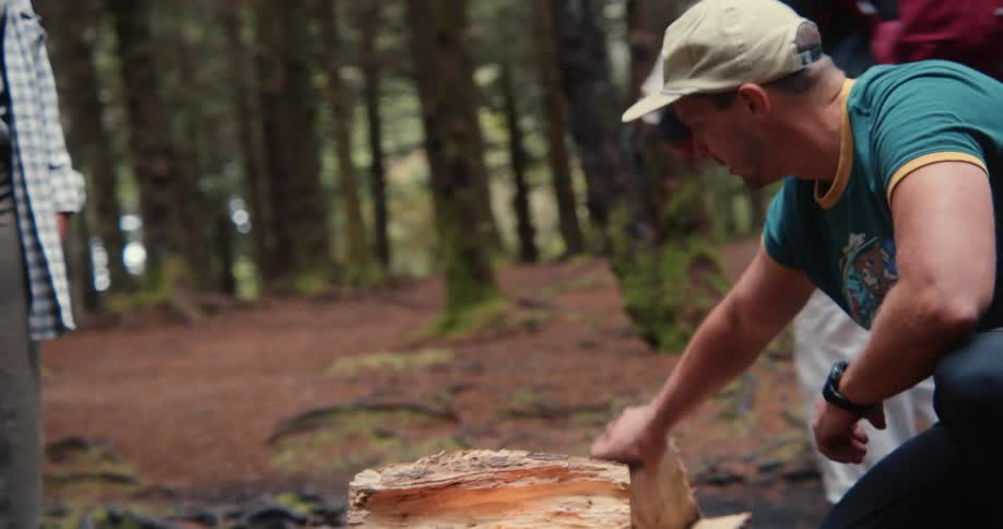Man placing firewood to start a campfire with his group of friends gathered around
