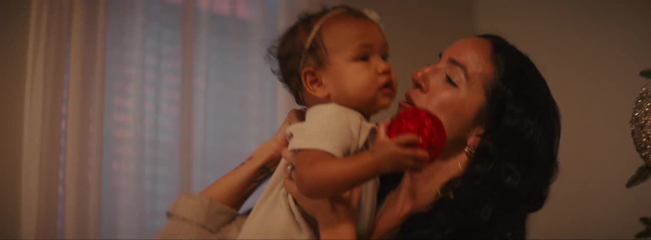 Joyful mother picking up the baby from the floor who is holding a christmas decoration and giving her a kiss