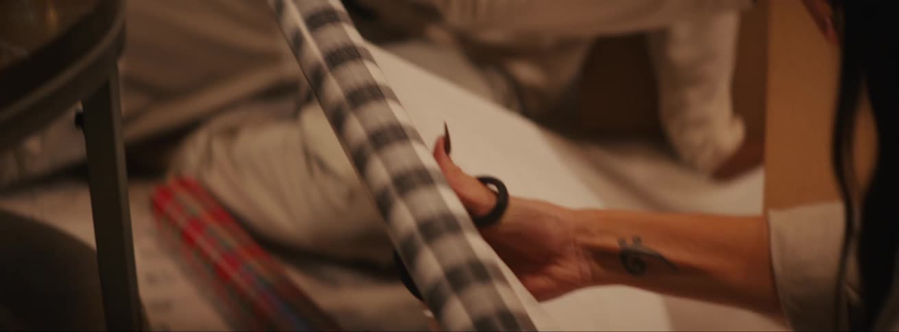 A woman cuts from a roll of wrapping paper while a man talks to her