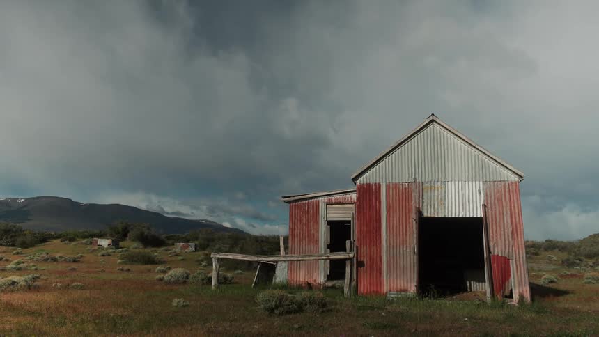 Opendoored ranch in the midst of a pasture with mountains on the horizon and a cloudy sky