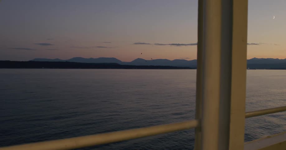 View from inside the boat to a seascape with a chain of mountains on the horizon under a reddish dawn sky