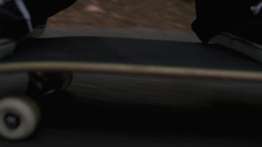 Closeup of a persons feet skateboarding on a street in the middle of a forest