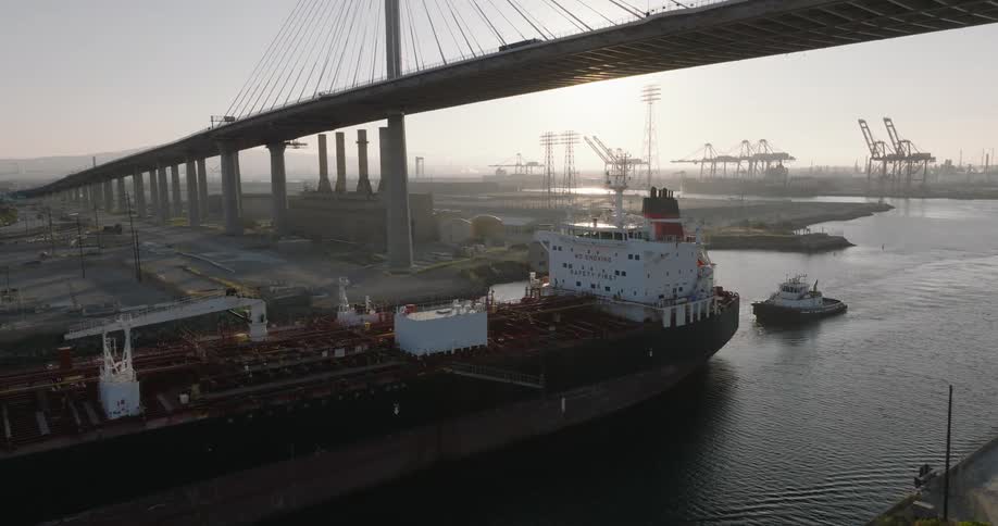 A huge cargo ship on top of the water and under a large bridge