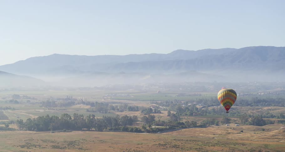 Hot air balloons flying over a small village in the countryside near mountains