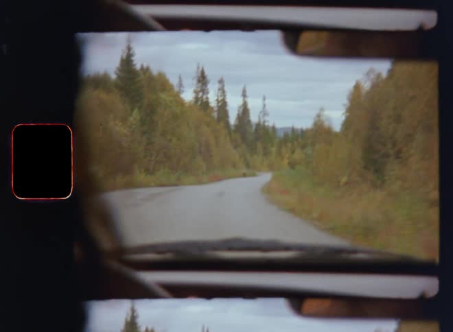 Unrecognizable woman or man drives along rural gravel road or windy street passing autumnal forest on an overcast day as the driver holds the steering wheel during a road trip adventure with mountains at the horizon on S8 film