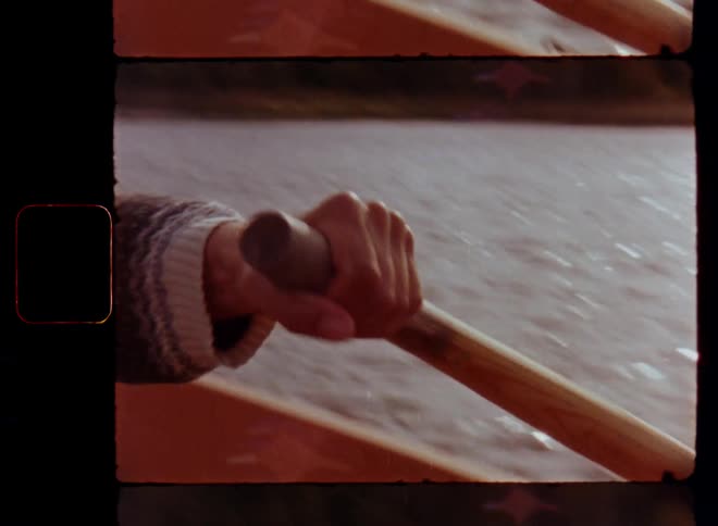 Super 8mm close-up of a bearded man contemplating and rowing an old boat holding the wooden oars or paddles with a firm grip in his hands on a sunny day with handheld camera movement