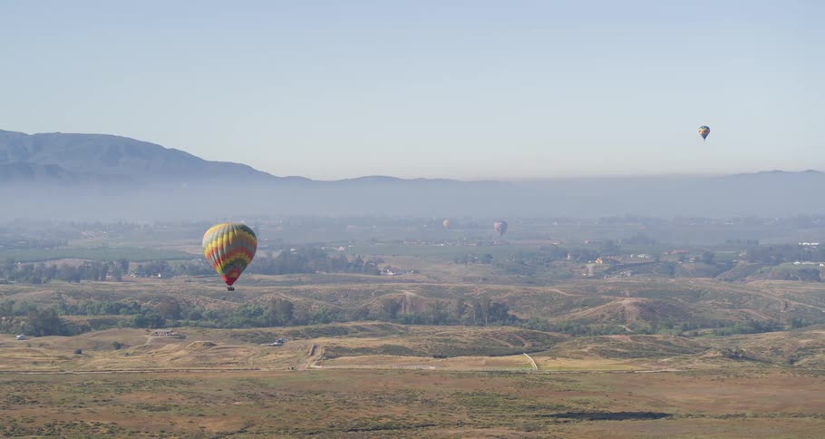 Panoramic aerial view of balloons flying over fields on a clear day