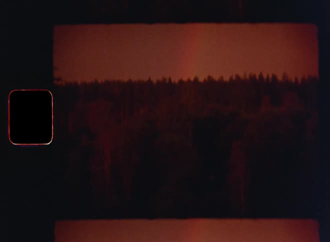 Retro view of a colorful rainbow behind a forest in front of a red or orange evening sky facing the river during the afterglow of a beautiful sunset