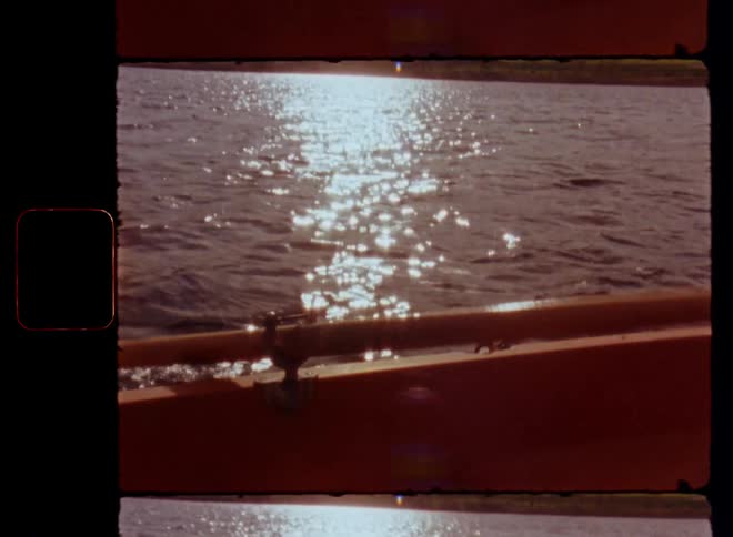 The bright sun of a sunny summer’s day shines onto the rippling surface of a lake as the hand of a person paddling a canoe or rowing boat holds the paddle or oar to move forward