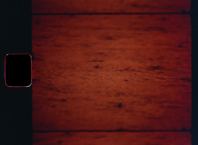 Drops of rain falling on the surface of a river or lake while the water moves due to waves and the red and orange evening sky reflects on the body of water caught on retro Super 8mm footage with vintage film burn