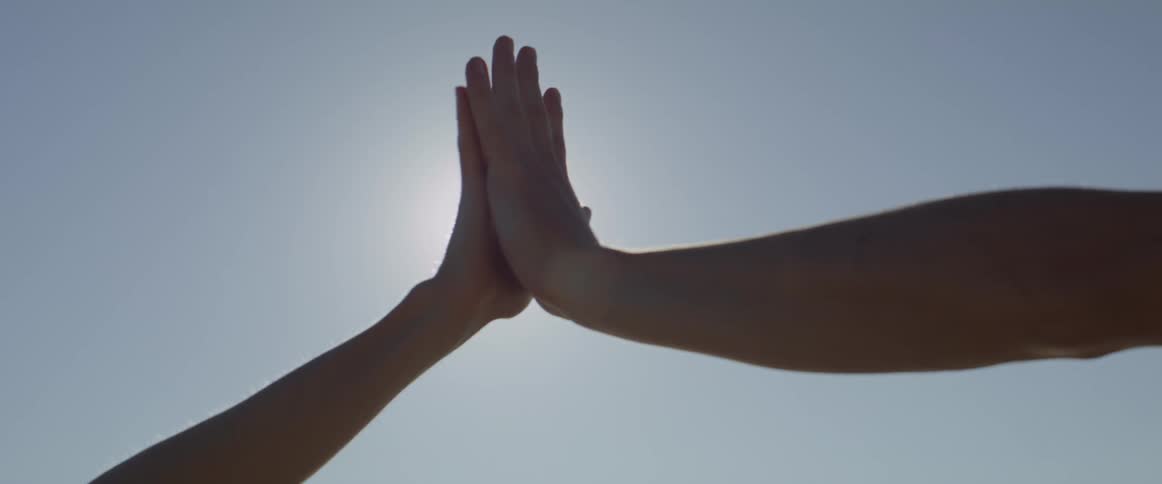 Hands of two people touching palms and interlocking with the sun in the background