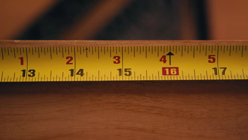 A yellow tape measure rolling out against the edge of a wood board