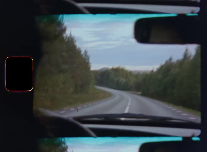 Unrecognisable female or male drives vintage car or vehicle holding the steering wheel with the hands along highway or curvy winding road through a conifer forest in a hilly country on a cloudy day on bumpy and shaky Super 8 film