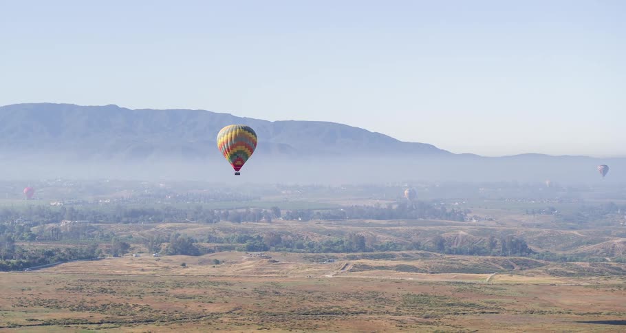 An aerial view from onboard a hot air balloon rising above the plains toward a mountain ridge in the daytime