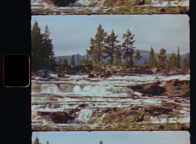 Water flows down river in a series of low waterfalls with hazy mountains in the background