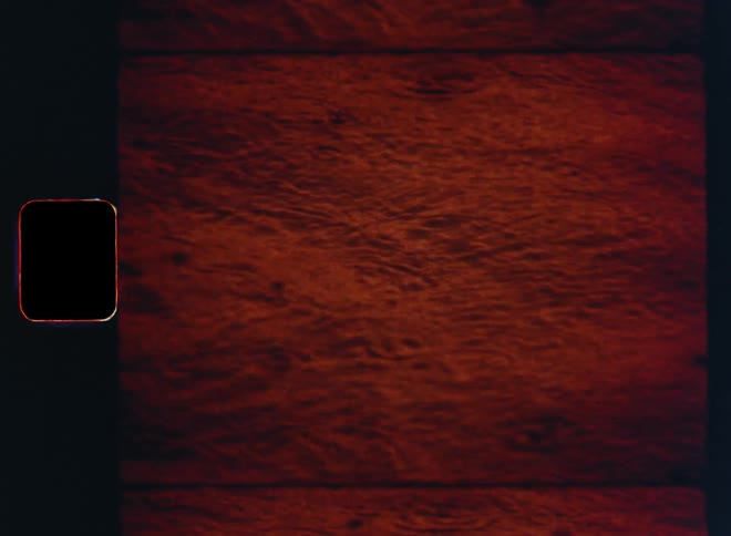 Heavy rain is falling onto the moving water and the rain drops splash into the rippling surface of the lake or sea while reflecting the red glowing evening sky with a vibrant red color on retro Super 8 film footage