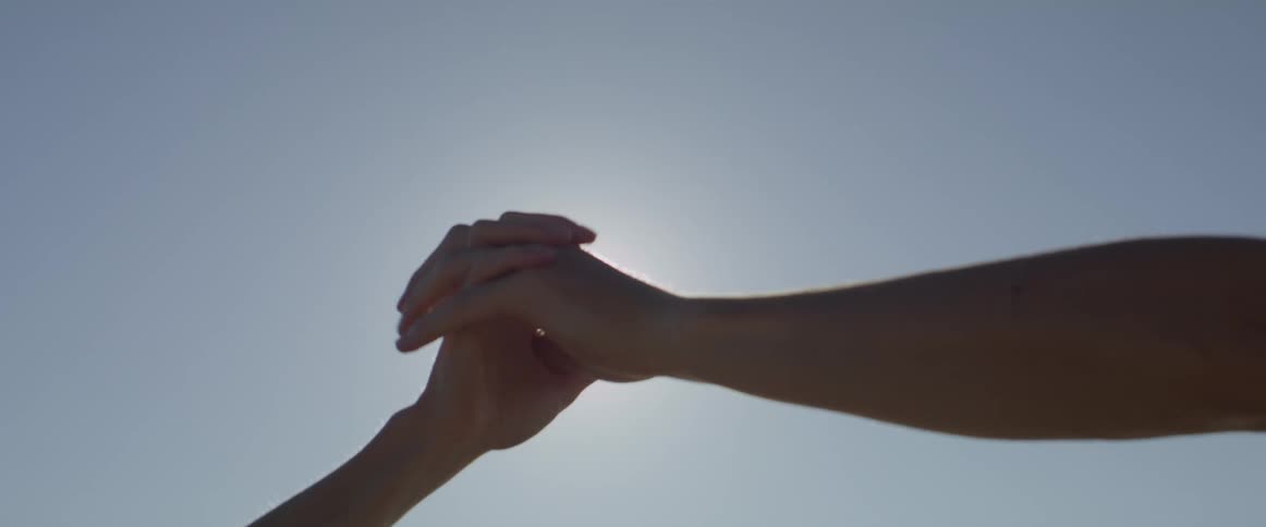 Couple touching hands intertwining fingers against a backdrop of a sunny sky