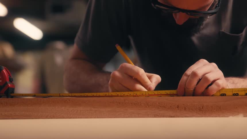 A clip of a carpenter measuring a hard wood with a tape