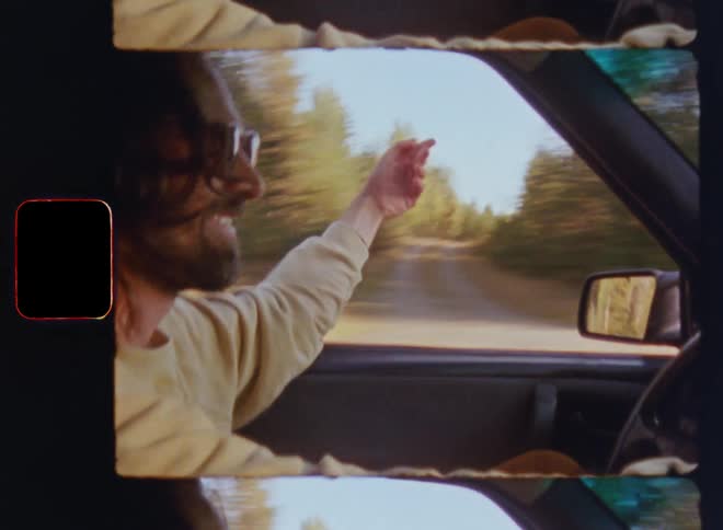 A smiling man happily cruising or driving his car on a forest country road passing by lots of trees enjoying the sun shine and the wind through his open window blowing and moving his long hair as he moves his arm and hand carefree in the fresh airflow