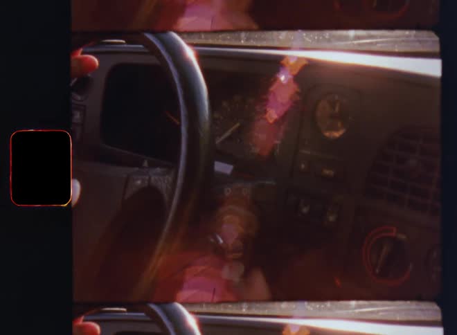A car interior dashboard of a vintage old-timer vehicle from the 1980s with steering wheel and speedometer being illuminated by bright sunlight causing lens flare and glare as the key is plugged into the ignition on retro film