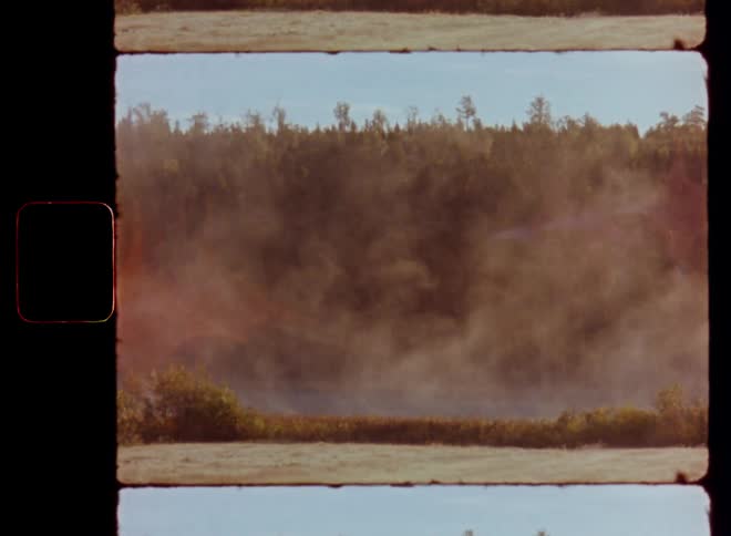 The early morning fog is rising up from the fields and lake in front of the forest as the sun rises on a sunny morning with beautiful weather on vintage S8 film