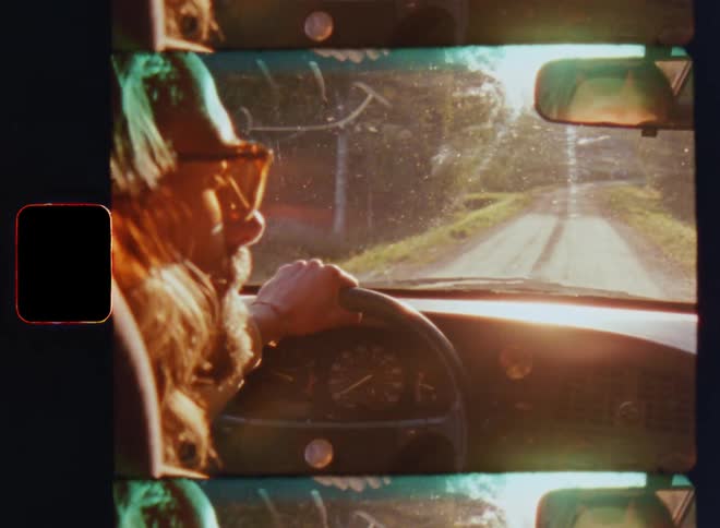 A brunette man with short beard driving his car on a sunny day on lonely gravel road into the setting sun through a forest as the bright sunlight of the warm summer morning causes glare and flare while he checks the exterior mirrors and looks around