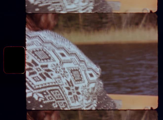 The strong hands of a man are holding the oars of a rowboat with a firm grip as he pulls the paddles towards his body while rowing over a lake on Super-8 film footage