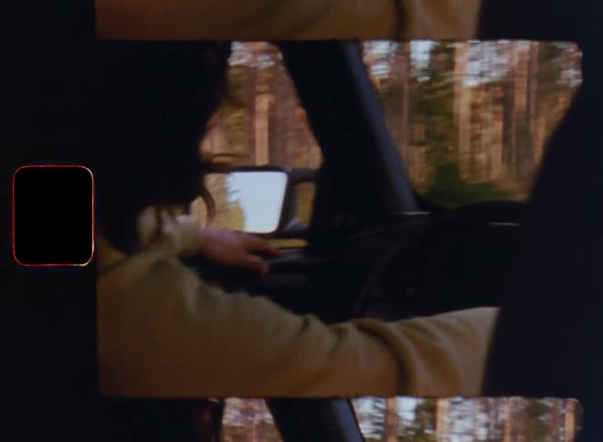 Unrecognisable young male with long brown hair short beard and yellow sweatshirt driving an old car through the forest as the warm evening sun shines on him and the trees and the bright blue sky reflects in the exterior mirror on a nice summer day