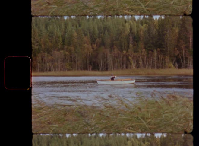 Idyllic film scene of an unrecognizable person or man that paddles his rowing boat on a small forest lake with a strong oar stroke caught on vintage film