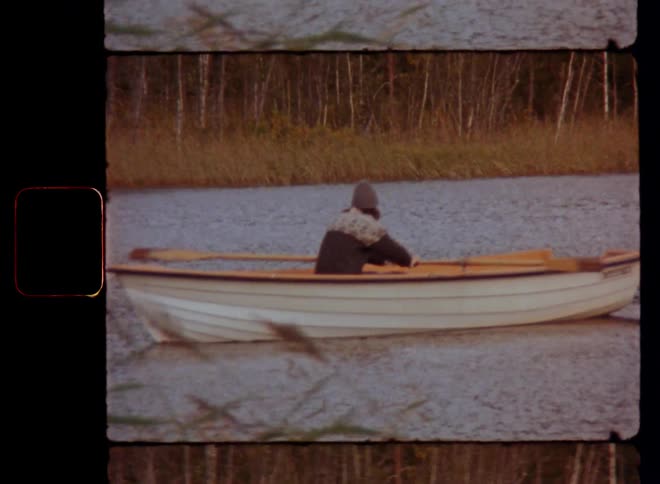 A man is rowing his old paddling boat downstream in a small river surrounded by cane and the reeds move or sway in the wind or breeze on a mild late summer or autumn day on the countryside enjoying nature and outdoor activities