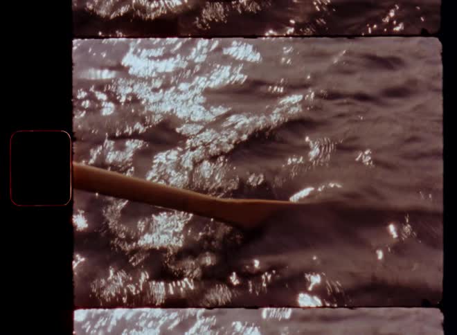 Super 8mm close-up of a wooden paddle or oar sinking into the water with a rippling surface reflecting the bright sunlight while paddling over a lake or river on a sunny day