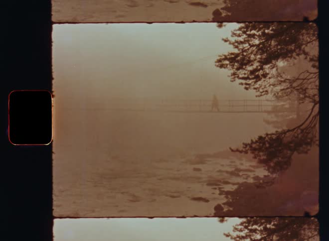 A person walks through the dense fog on a hanging bridge over a fast flowing river
