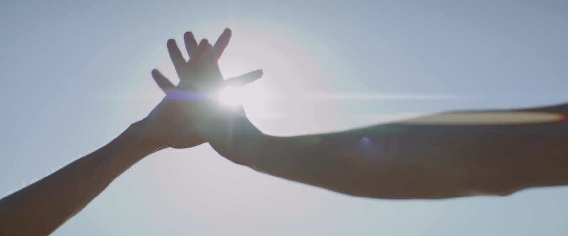 Couple touching hands intertwining fingers against a backdrop of a bright sunny sky