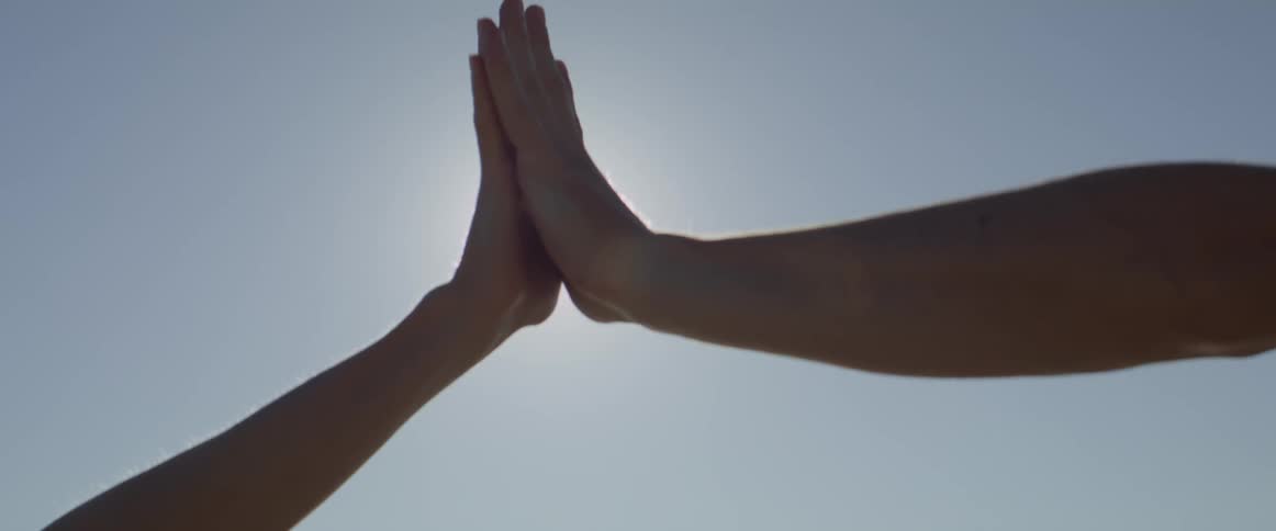 Hands touching and fingers interlocking with the sun shinning through briefly between them under a clear light bluepurple sky