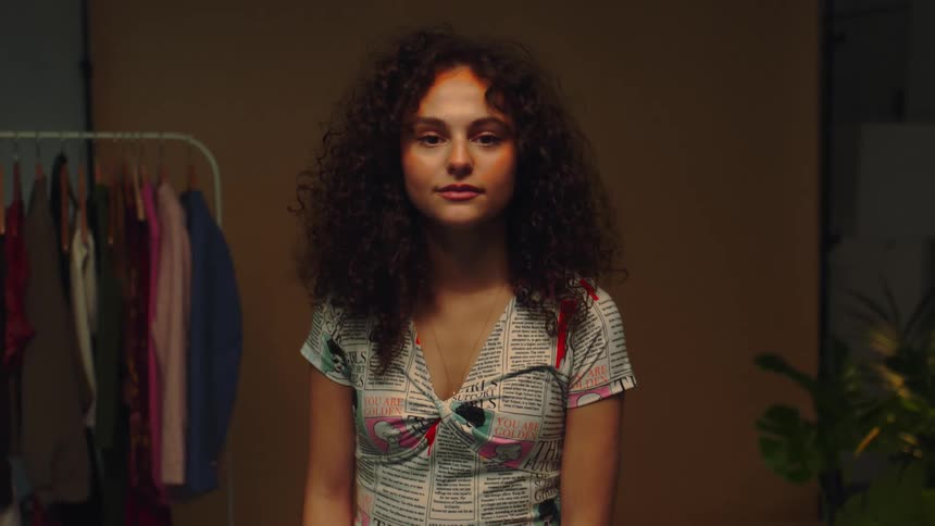 A young woman with very curly hair turns her head to look at the camera
