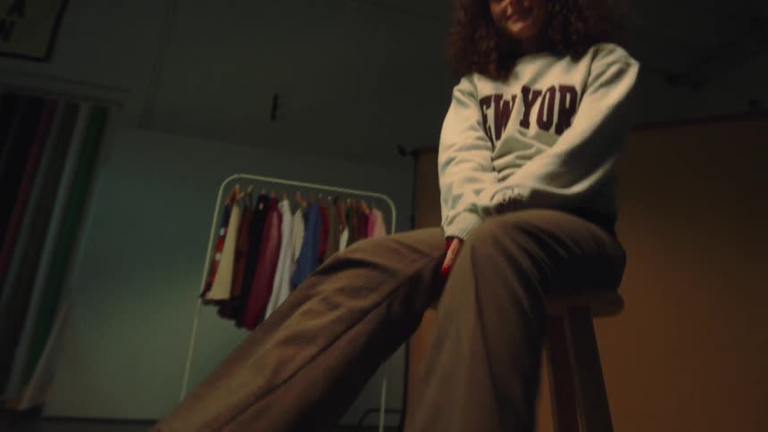 A woman sitting on a stool swinging her legs and she is wearing brown formal boots