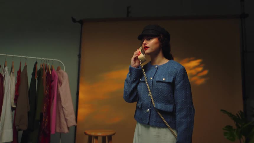 Model standing in room with clothes rack talks on the phone