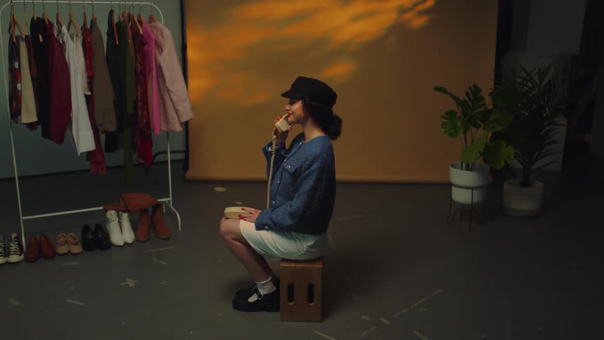 Model in a studio sitting on a box talking on a corded telephone