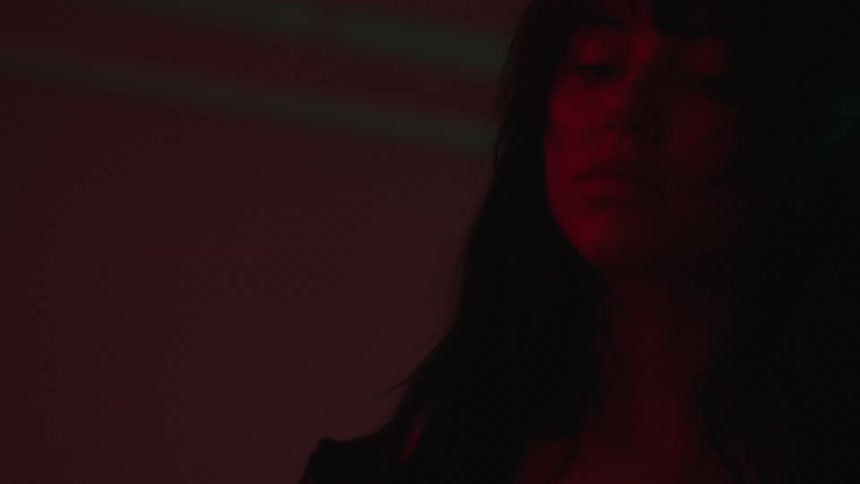 A woman with a black blouse and a tattoo dances in red lighting