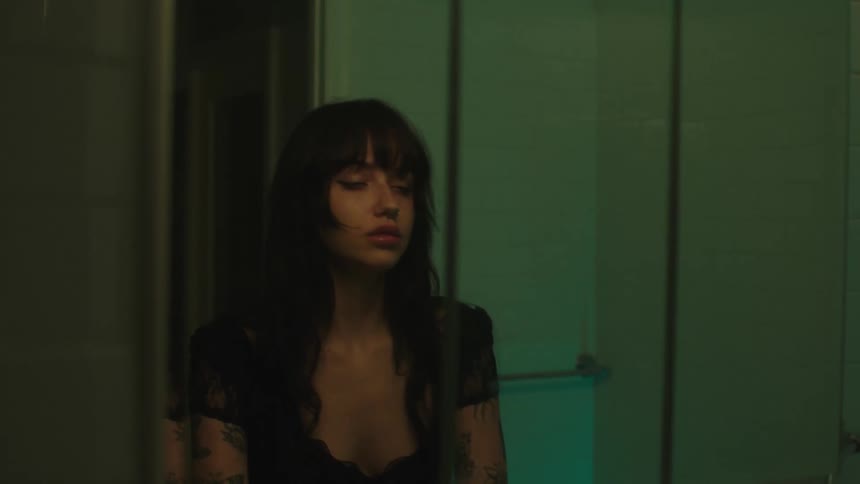Tired young woman applying lip gloss in front of a bathroom mirror