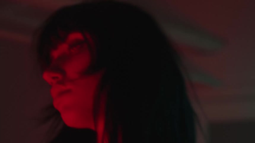 Portrait of a young woman dancing with her hands on her head and red lights under her face