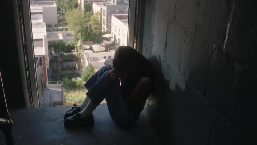 Teen sits at the entrance with her back against the wall and her head rested on the kneel