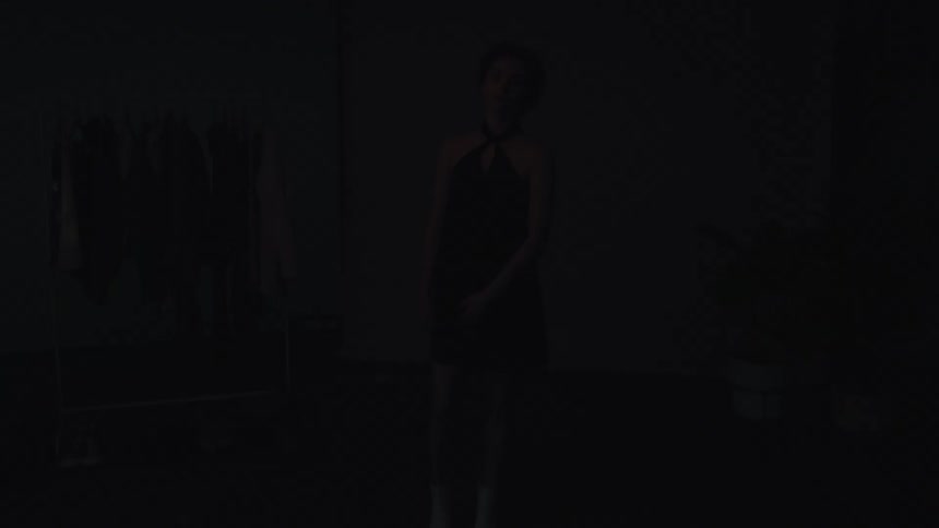 Female model posing in a green dress in a dark room with lighting passing under her