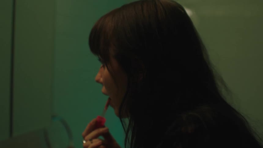 A drunk woman applying lipstick looking in the mirror