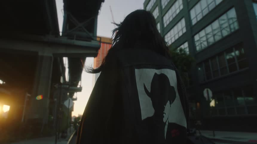 Woman walking away on the sidewalk of a metropolis with the sun on the horizon