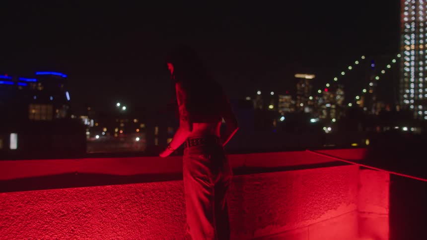 A woman stands on the roof of the building bathed in the glow of red light at night