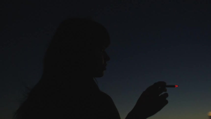 A female at the roof of a building smoking with the city view in sight