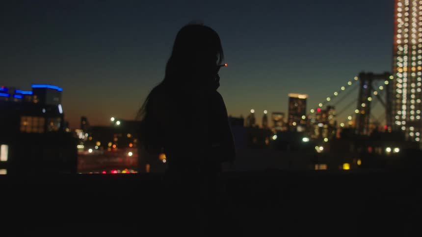 A woman smoking a cigarette on top of a building in the city